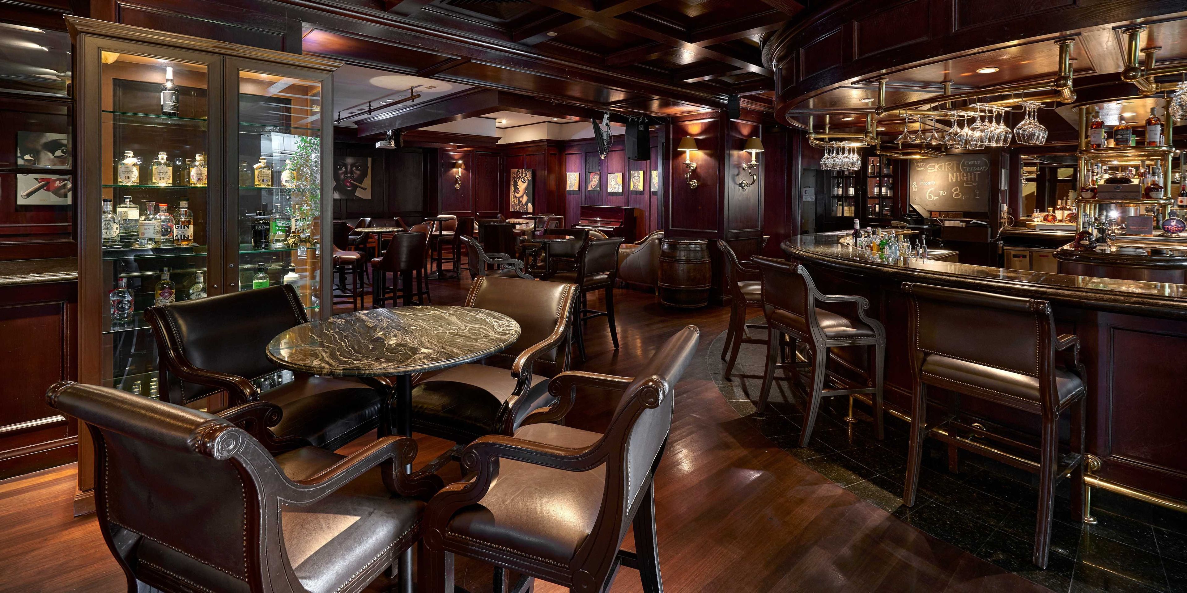 A bar area with leather chairs, a marble table, and a bar counter with bottles.