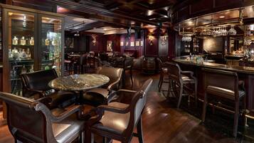 A bar area with leather chairs, a marble table, and a bar counter with bottles.