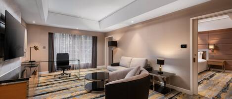 Una habitación de hotel moderna con una televisión de pantalla plana, un sofá, un escritorio con lámpara y una alfombra estampada.