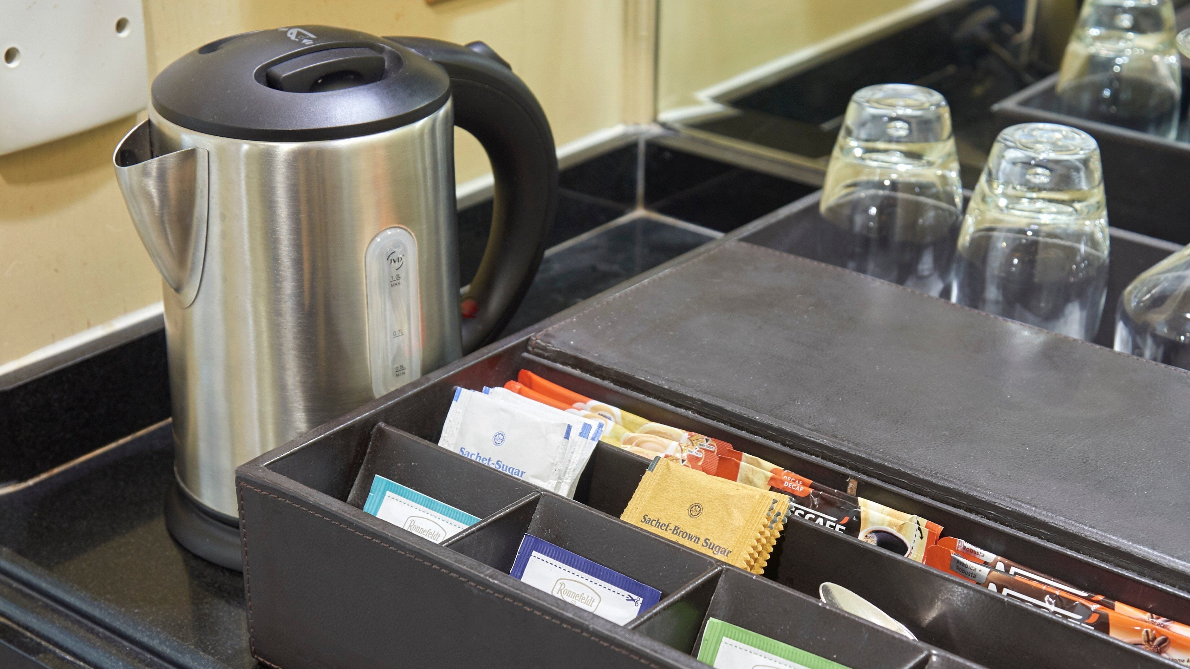 A kitchen area with a stainless steel kettle, a coffee machine, and a coffee dispenser with various coffee pods.