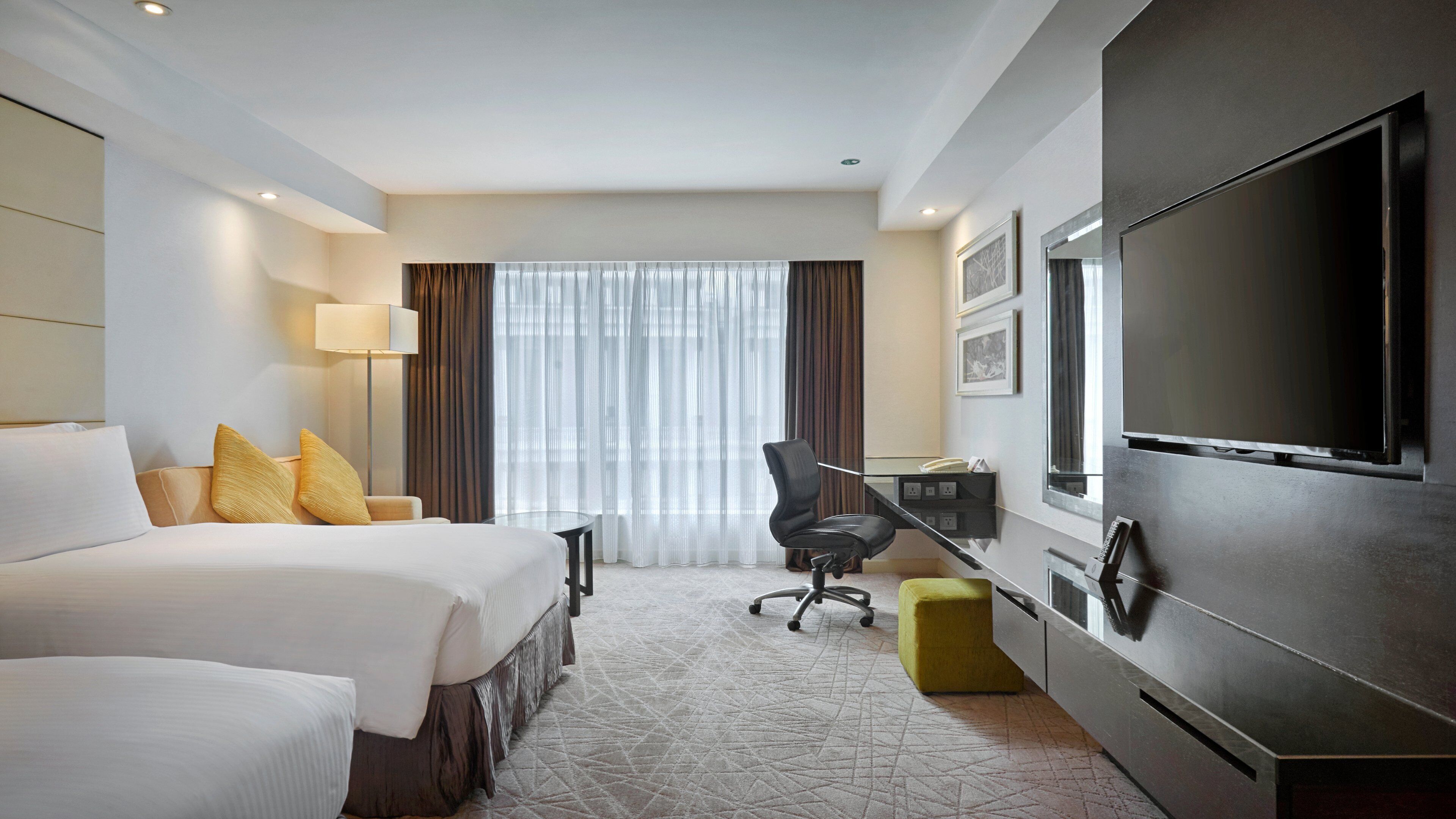 Une chambre d’hôtel équipée d’un lit, d’un bureau, d’une chaise, d’une télévision et d’une fenêtre avec des rideaux.