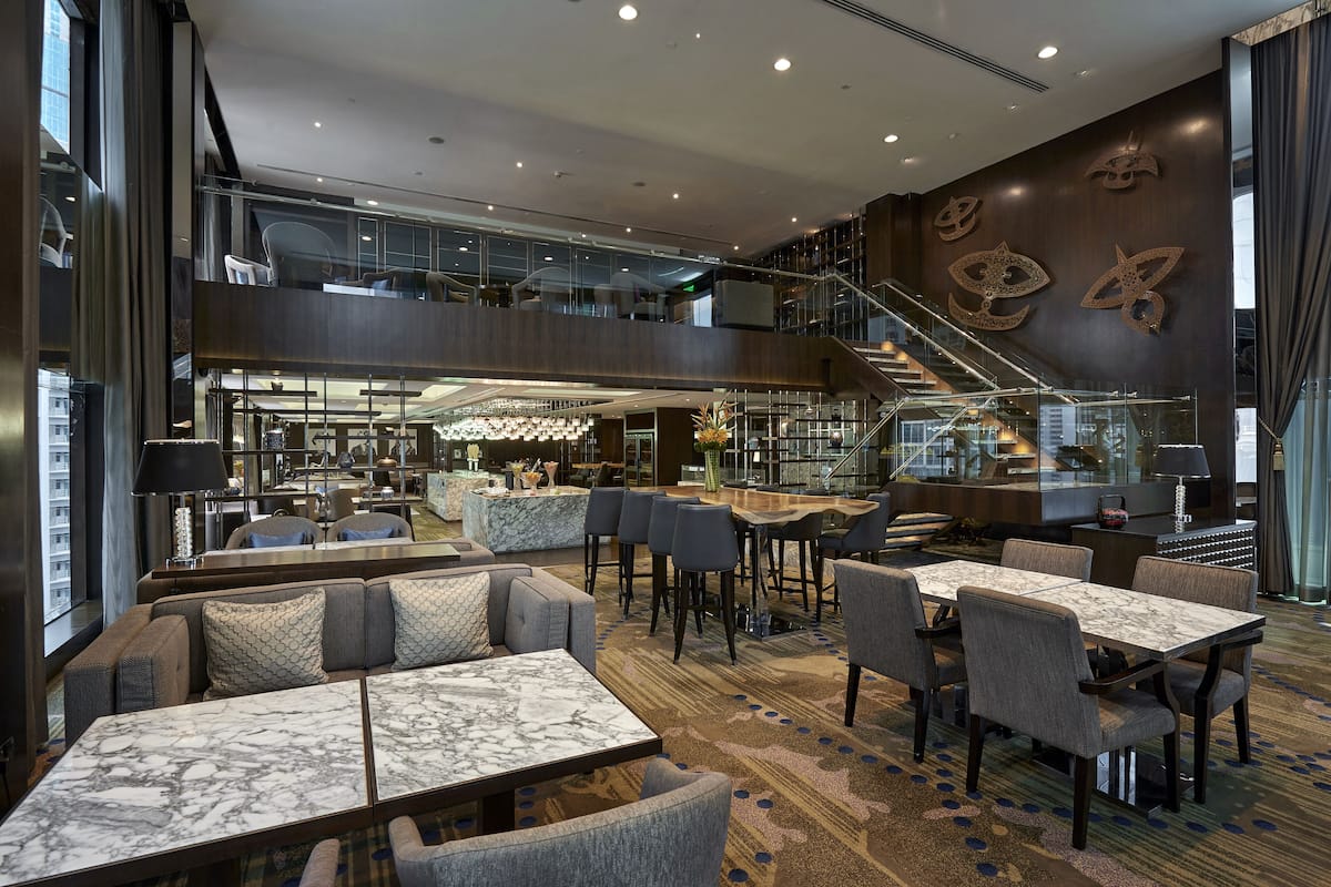 A modern hotel lobby with a mezzanine level, seating areas, a staircase, and a bar.