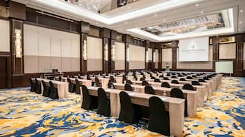 A conference room with rows of tables and chairs, a large screen, and a patterned carpet.
