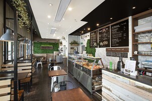 A cafe interior with wooden tables and chairs, a counter with a menu, and a green wall with plants.