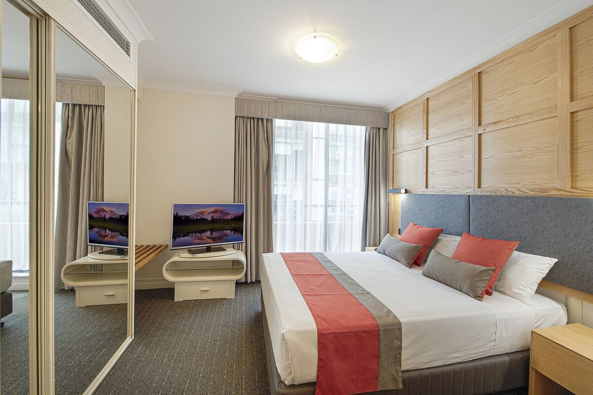 A hotel room with a large bed, a desk with a TV, a mirror, and a window with curtains.
