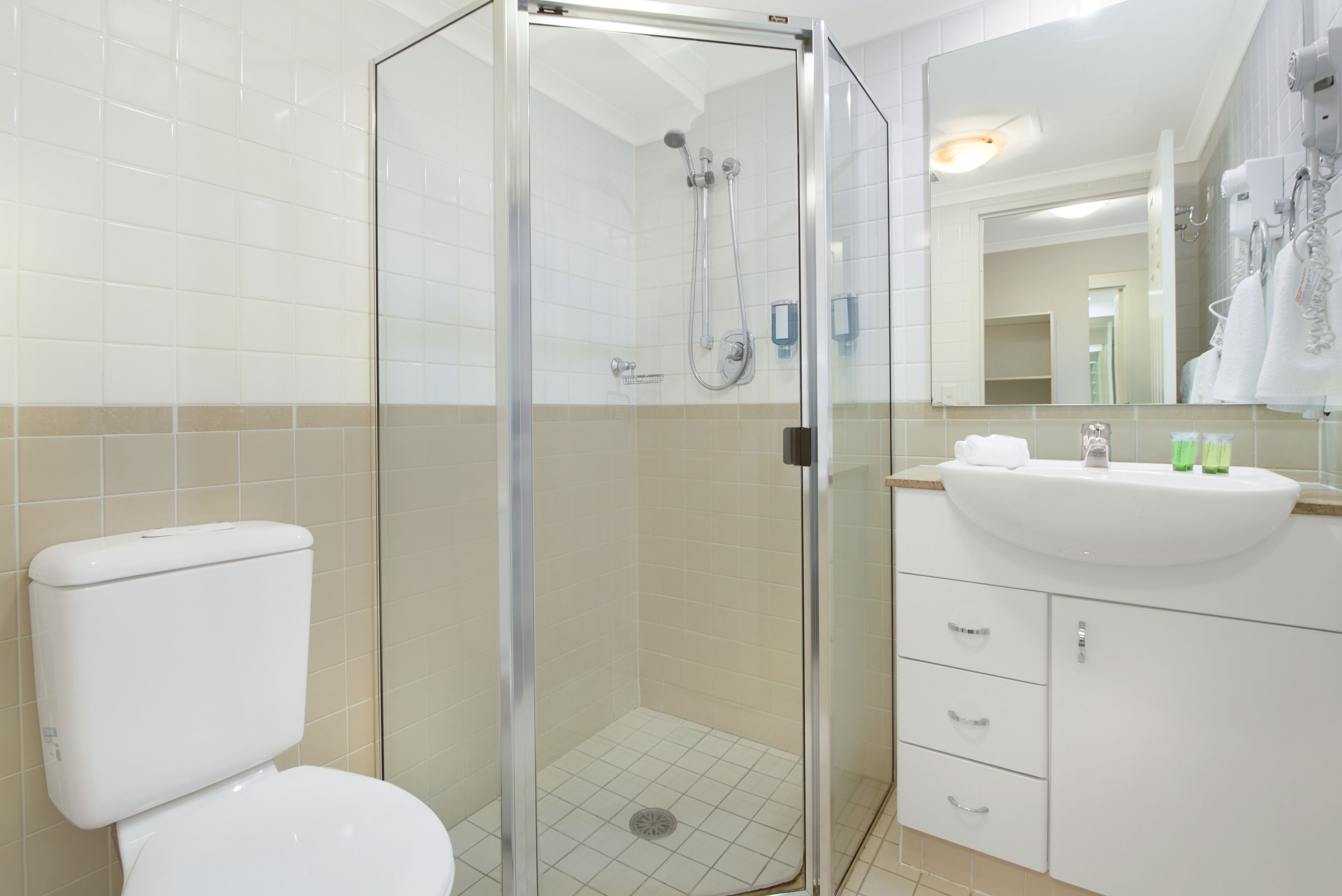 A modern bathroom with a glass-enclosed shower, a white toilet, and a sink with toiletries.