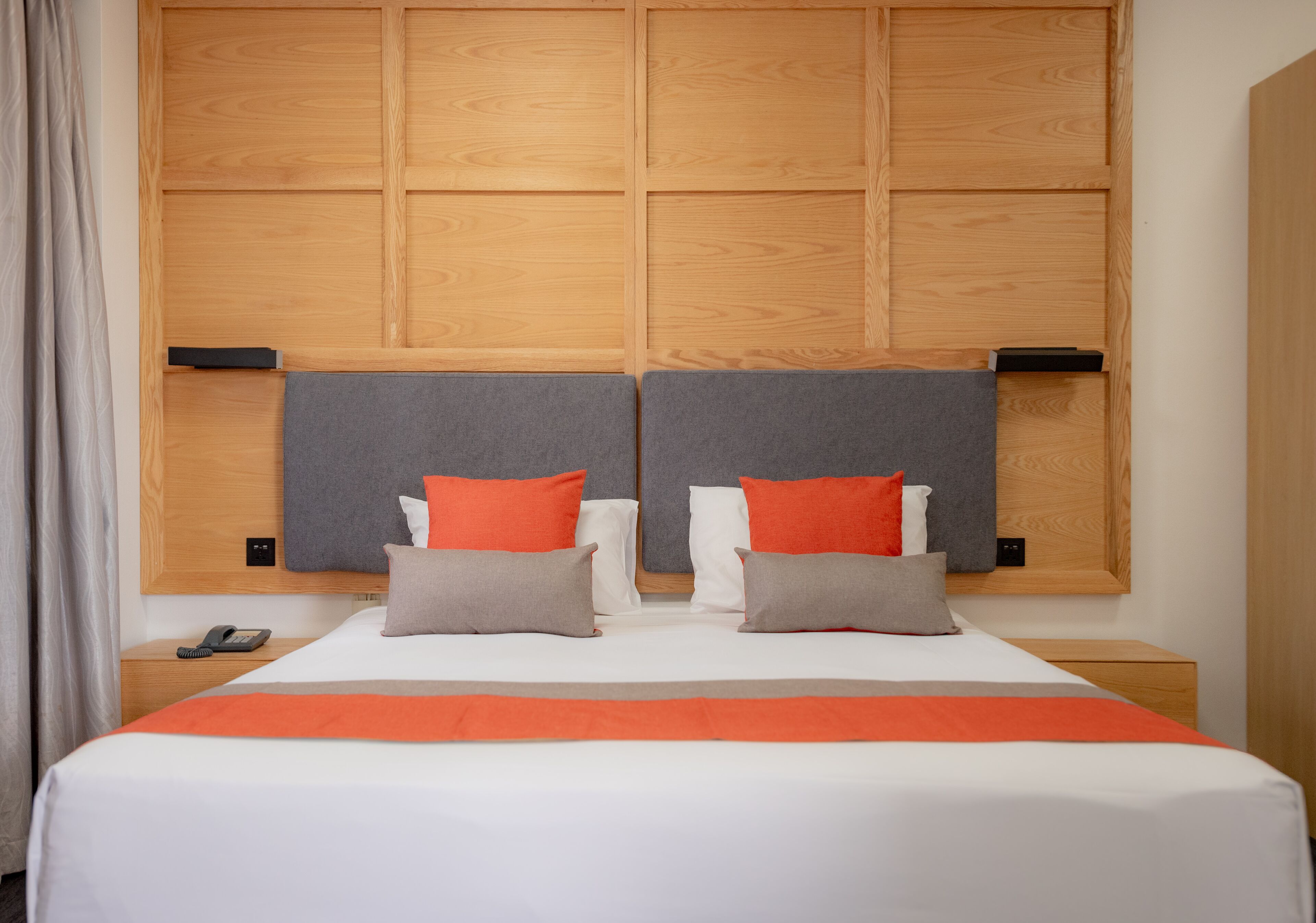 A hotel room with a large bed, two nightstands, a wooden headboard, and a telephone on the left nightstand.