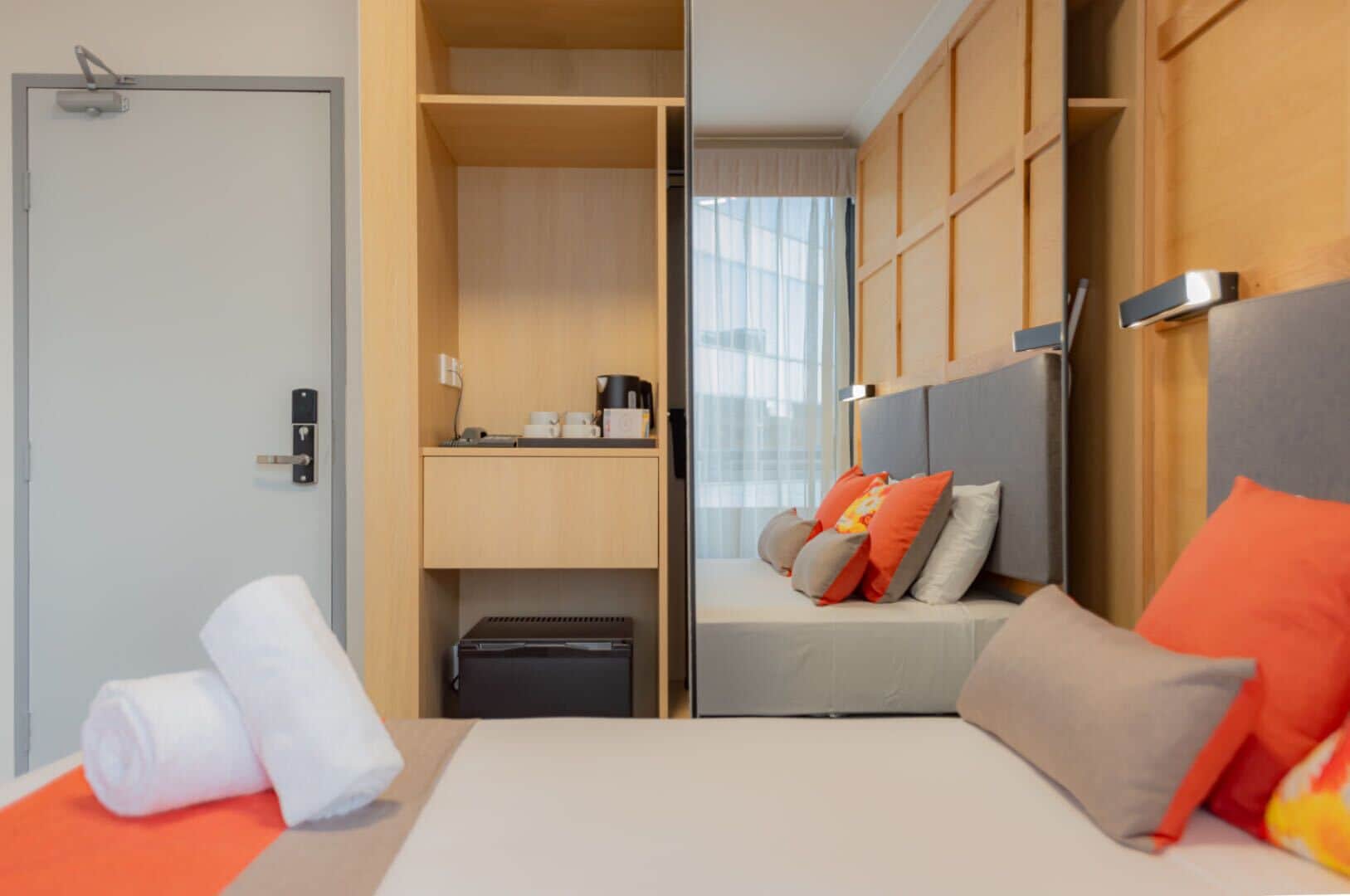 A hotel room with a bed, a desk, a wardrobe, and a window with curtains.