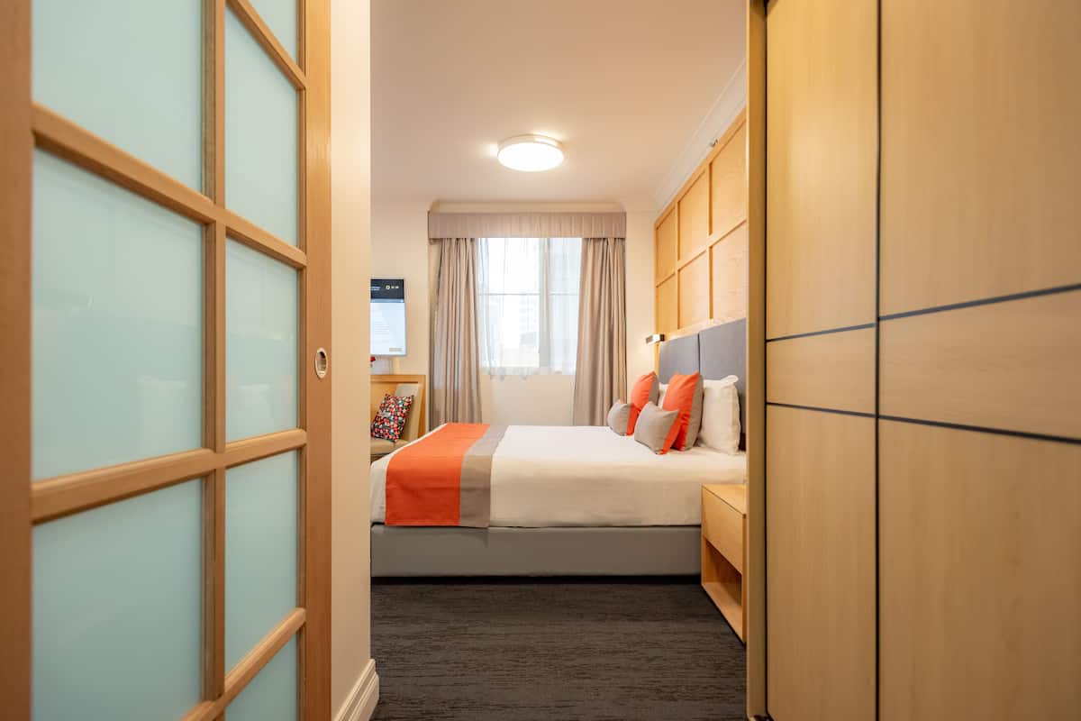 Ein Hotelzimmer mit Bett, Nachttisch, Kleiderschrank und einem Fenster mit Vorhängen.