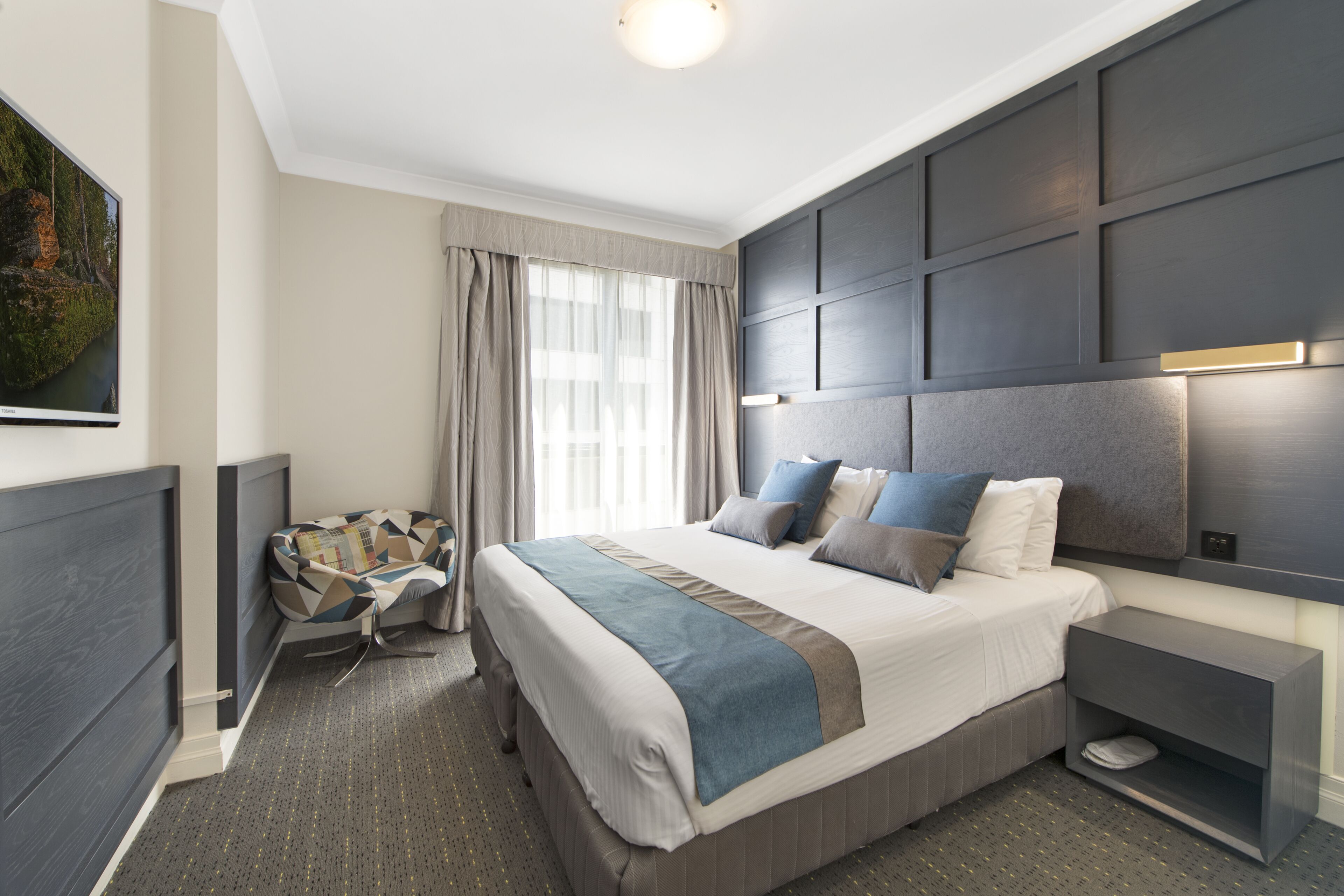Une chambre d’hôtel moderne avec un grand lit, une table de chevet, une télévision et une vue sur l’extérieur.