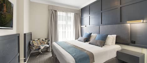 A modern hotel room with a large bed, a bedside table, a TV, and a view of the outdoors.