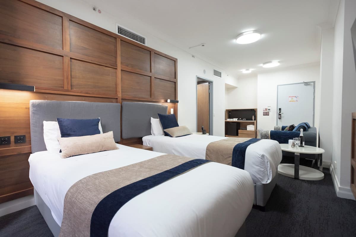 Ein Hotelzimmer mit zwei Betten, einem Holzkopfstück, einem runden Tisch und einem Spiegel.