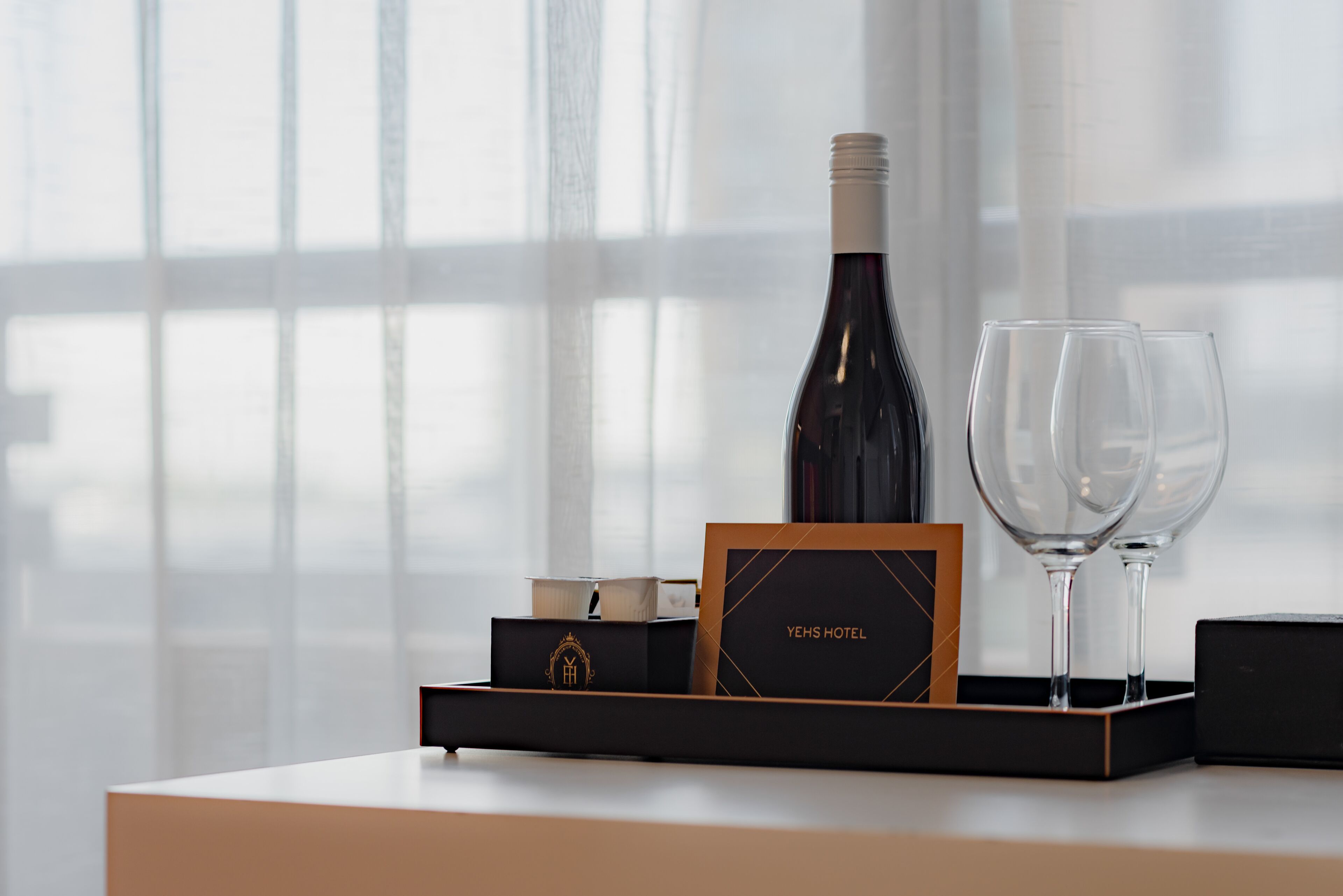 Una botella de vino, dos copas y una caja con la marca, todo sobre una bandeja.