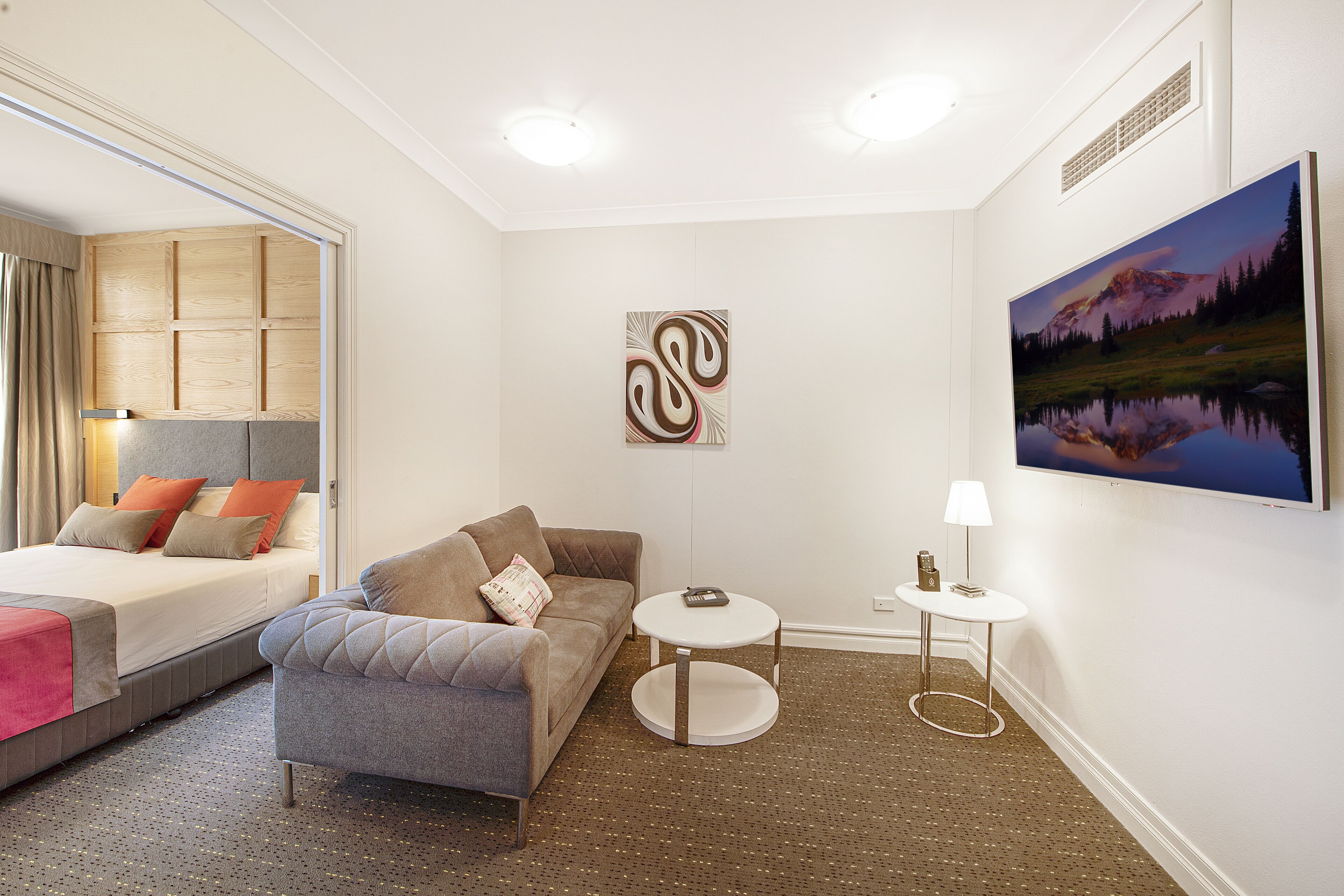 Una habitación de hotel moderna con una cama, un sofá, una pequeña mesa redonda y un cuadro en la pared.