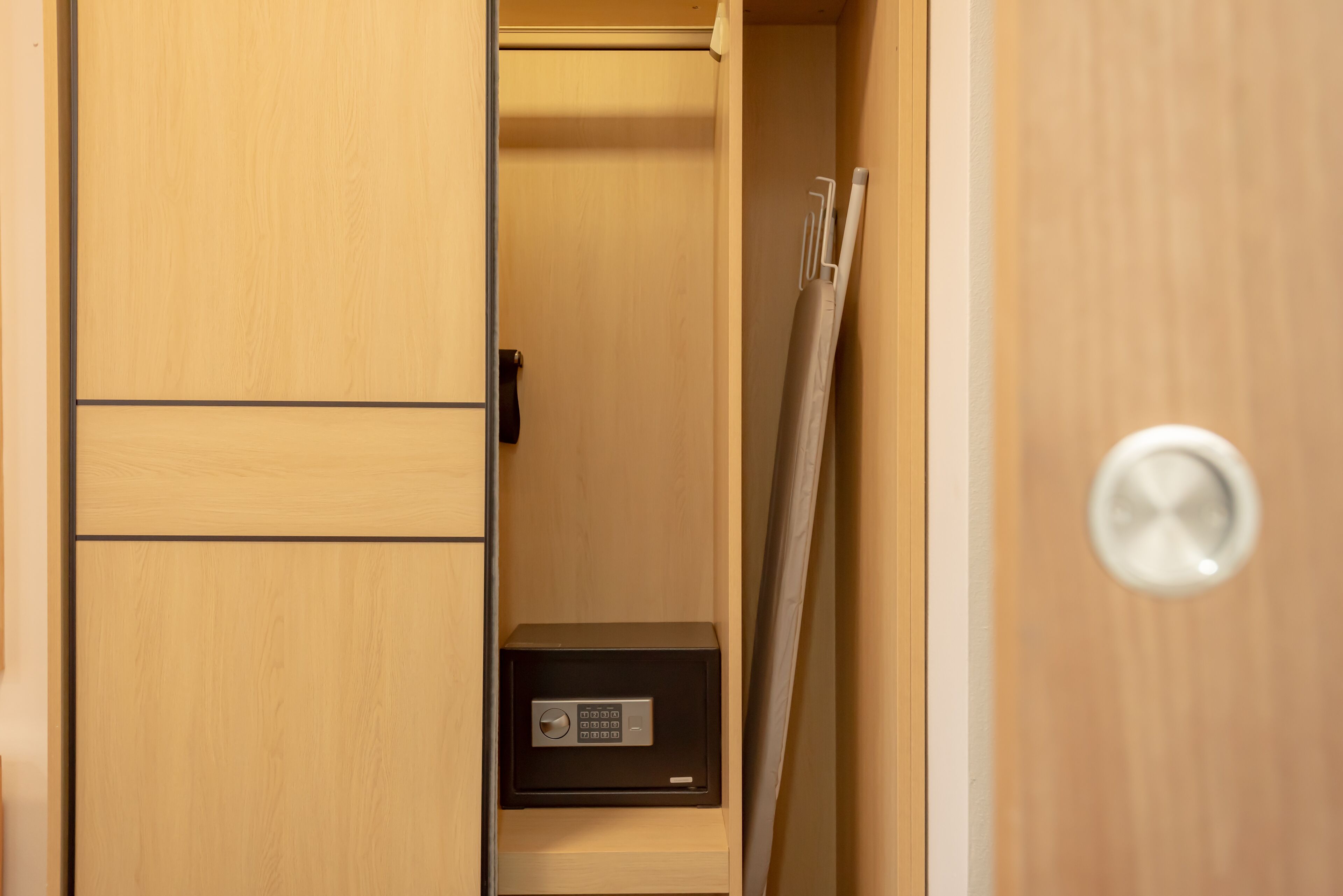 A wooden wardrobe with a black safe, a towel, and a door handle.