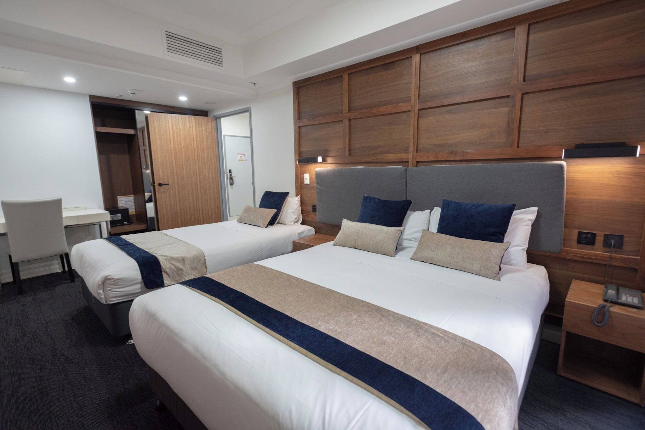 A hotel room with two beds, a desk, and a wardrobe.
