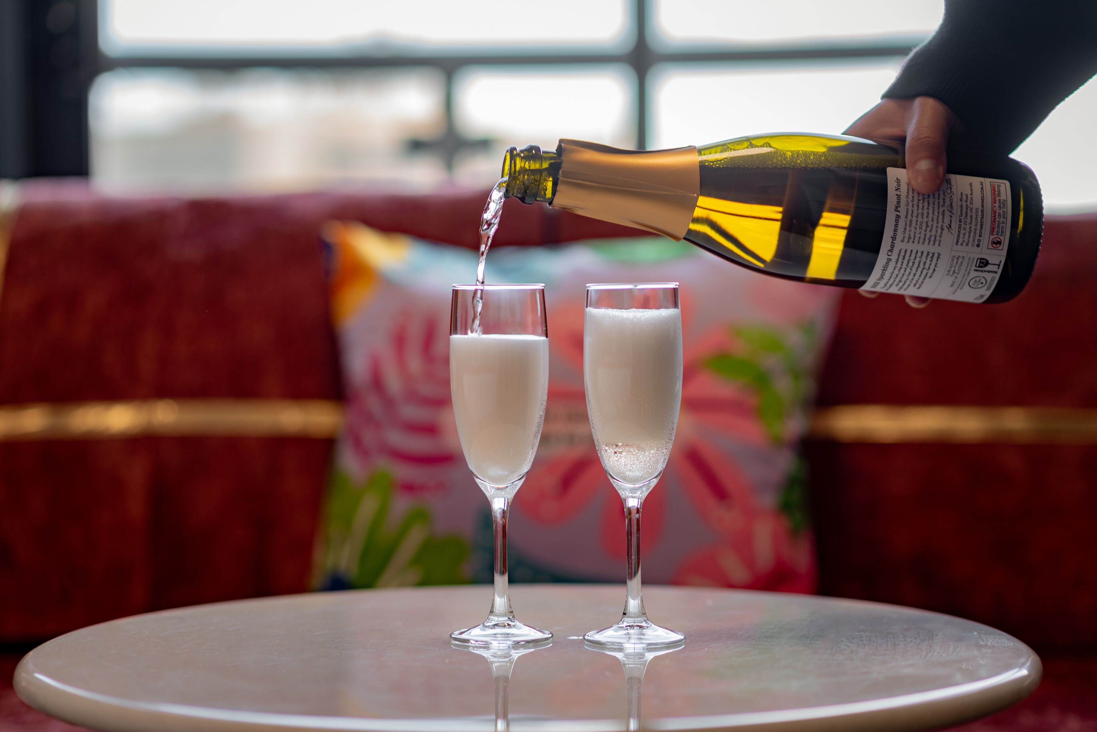 A bottle of champagne being poured into two glasses on a table.