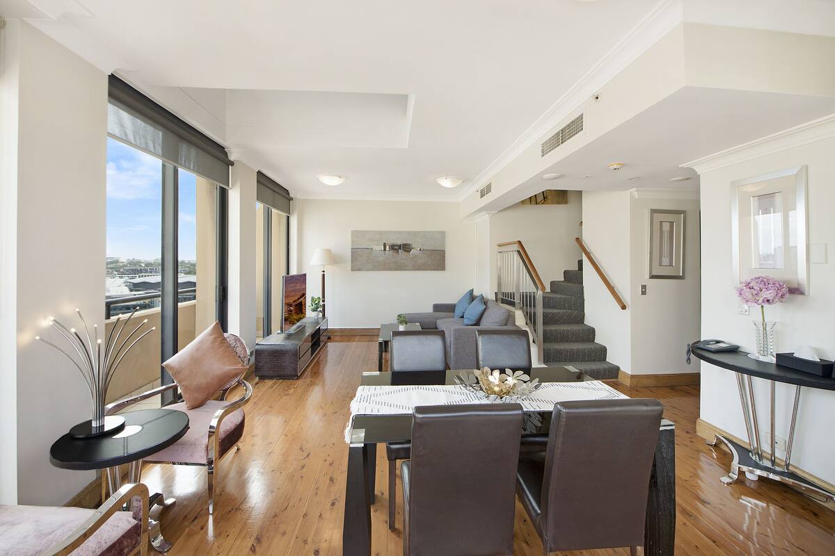 A spacious living area with a dining table, chairs, a sofa, and a staircase leading to an upper floor.