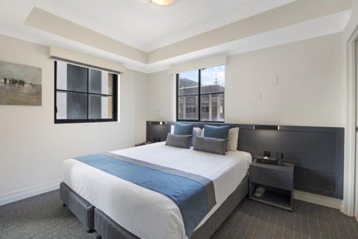 Habitación de hotel moderna con una cama grande, dos mesitas de noche, una ventana y un cuadro en la pared.