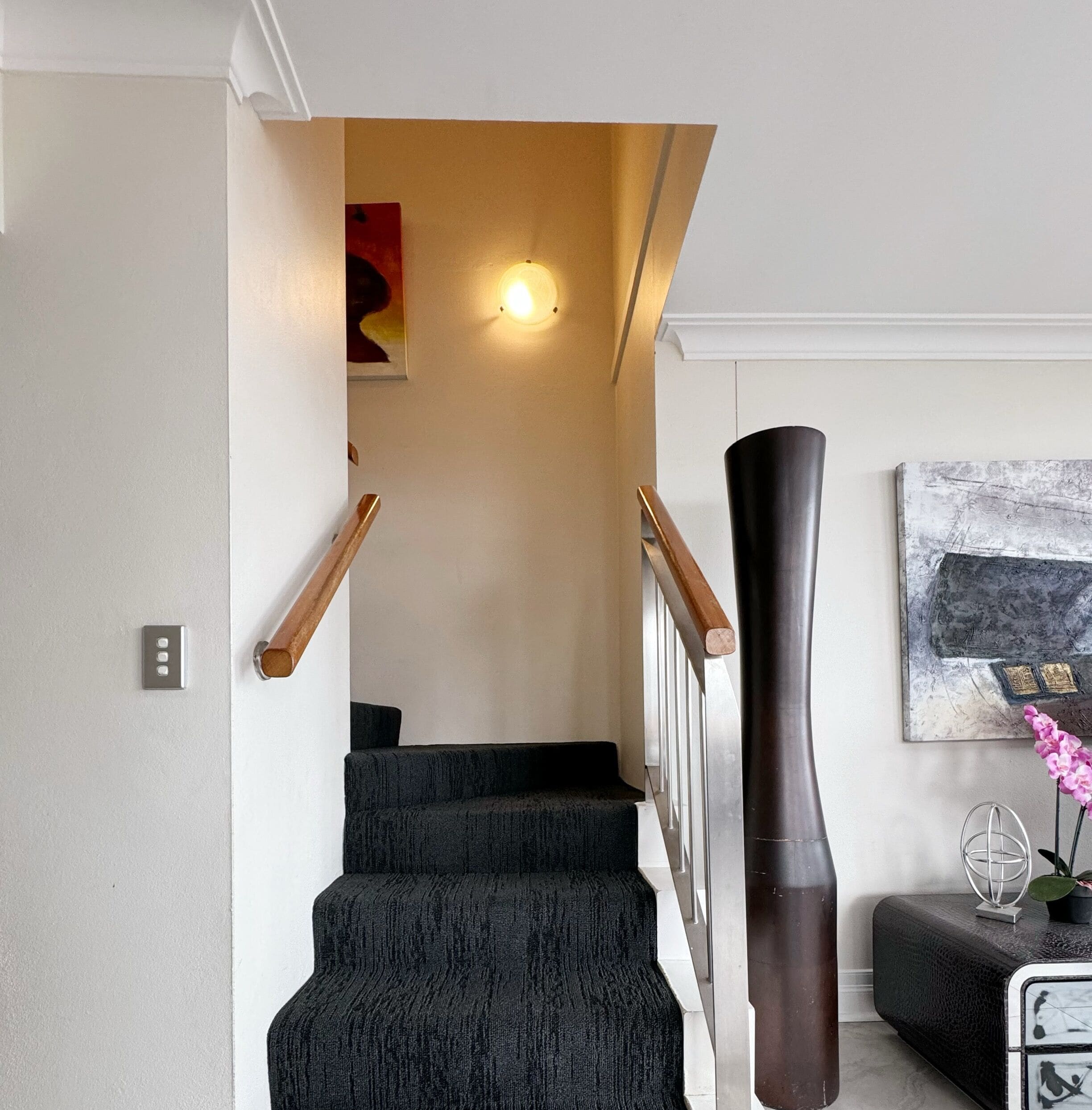 A staircase with dark steps, wooden handrails, and a wall-mounted light fixture.