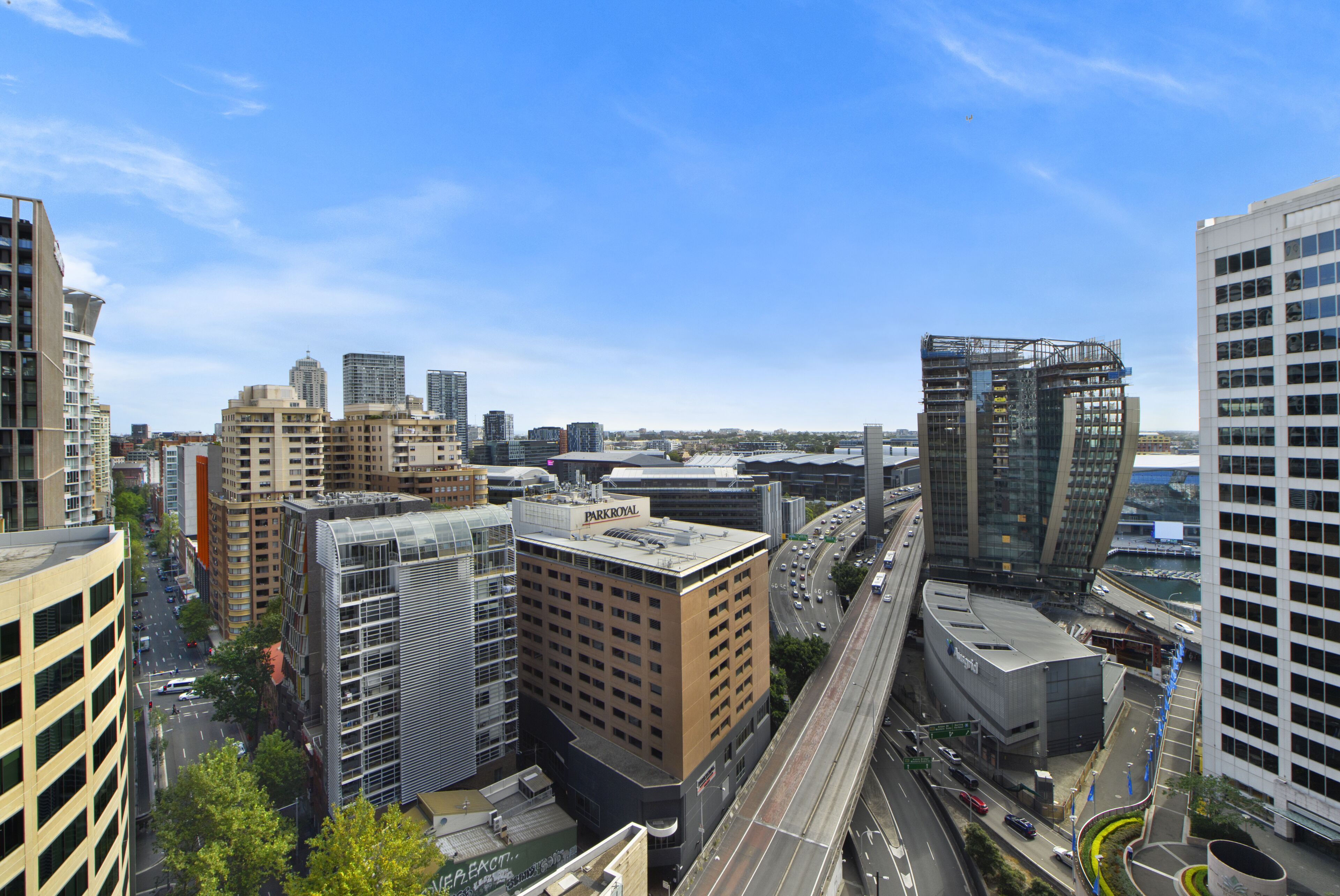A high-rise building with a prominent 'PARKROYAL' sign, surrounded by other tall buildings and a busy road with vehicles.