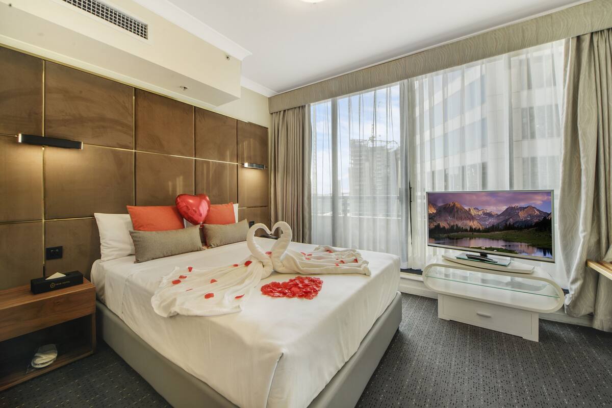 A modern hotel room with a large bed, a TV, and a scenic mountain view.