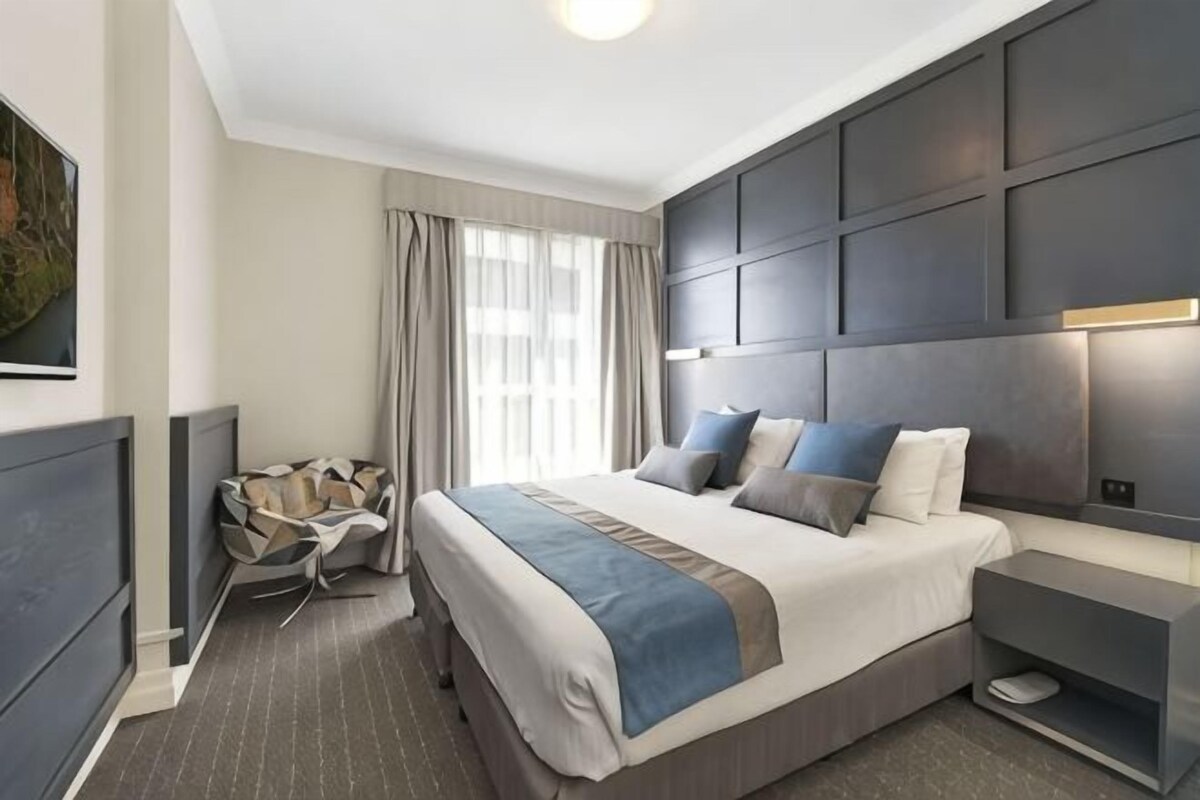 Ein modernes Hotelzimmer mit einem großen Bett, Nachttischen, einem Schreibtisch und einem Sessel.