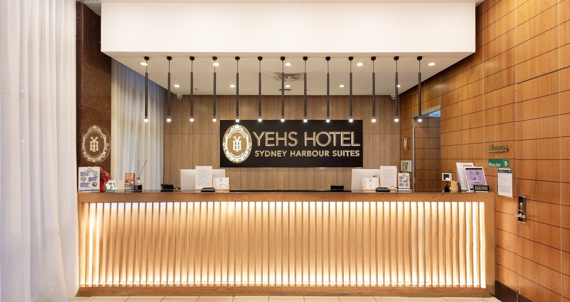 A reception desk at YeHs Hotel with a modern design, featuring a wooden reception desk, a signboard with the hotel name, and a first aid sign.