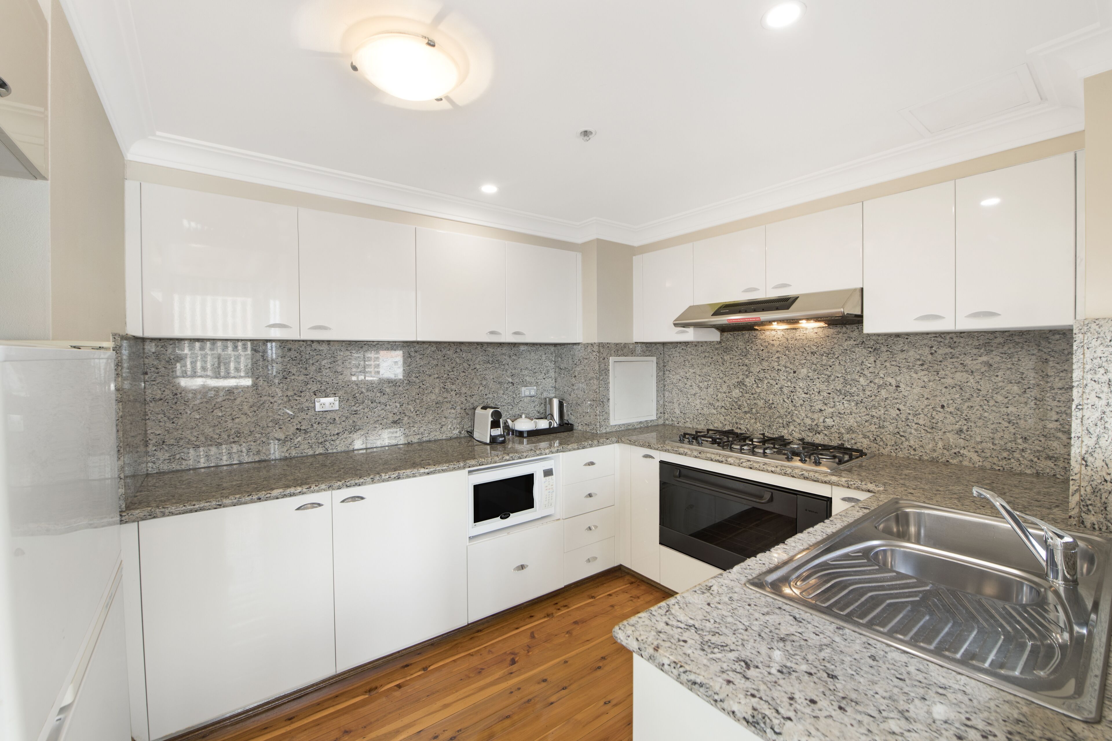 A modern kitchen with white cabinets, granite countertops, a built-in microwave, stove, and sink.