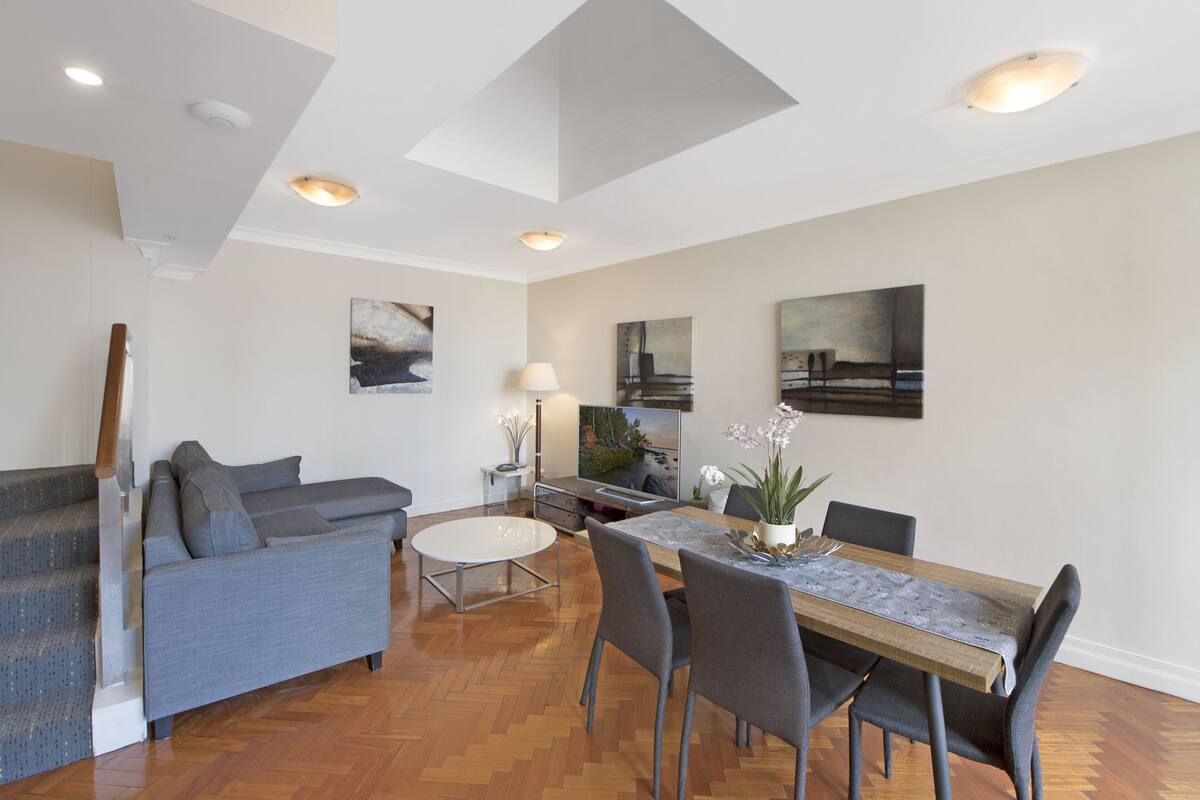 A modern living room with a grey sofa, a dining table with chairs, and artwork on the walls.