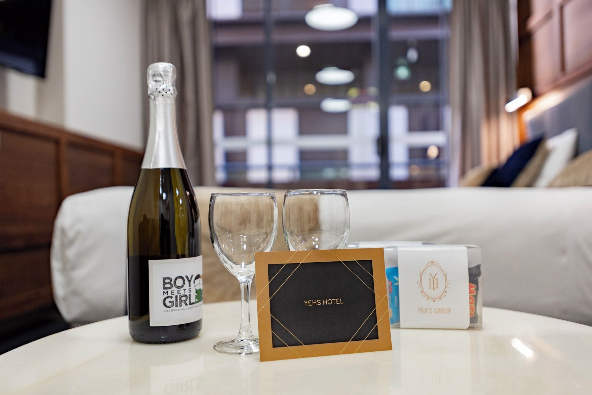A bottle of wine, two glasses, and a hotel name card on a table in a hotel room.