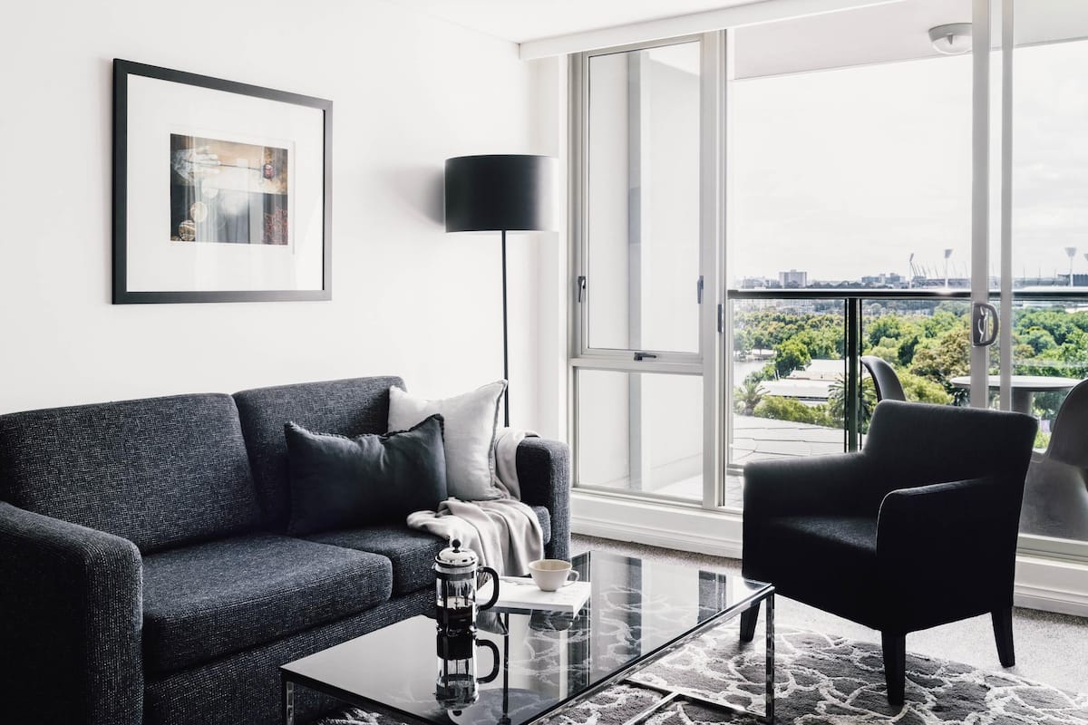 Un salon moderne comprenant un canapé, une table basse, un lampadaire et une grande fenêtre donnant sur la ville.