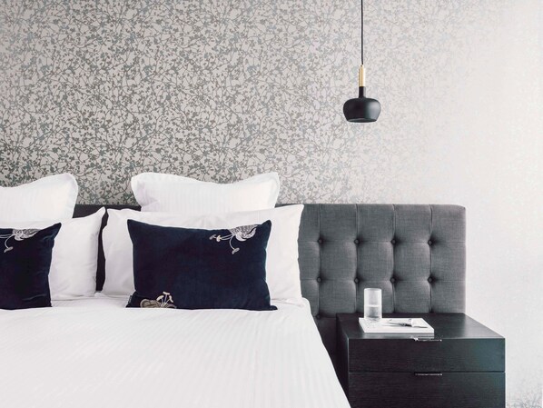 A bedroom with a tufted headboard, a bedside table with a glass and a book, and a floral-patterned wallpaper.