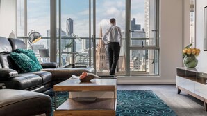 Una sala de estar moderna con un amplio ventanal, un sofá de cuero, una mesa de centro y vistas a un paisaje urbano.