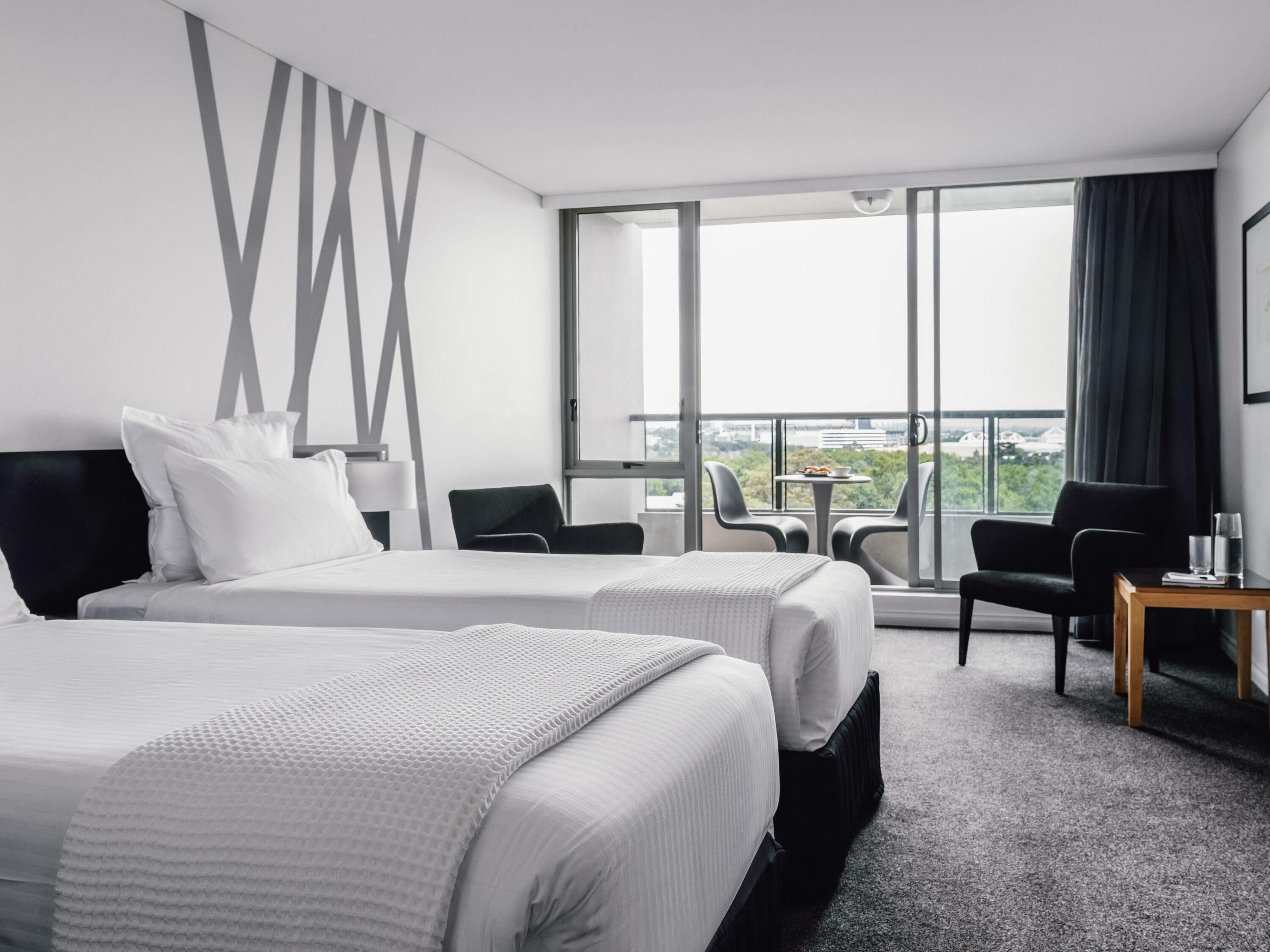 Une chambre d’hôtel avec deux lits, un balcon offrant une vue et une petite table avec des chaises.