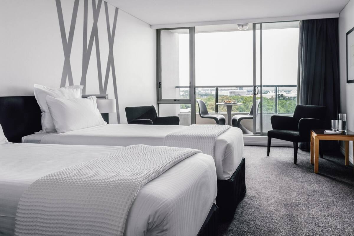 A hotel room with two beds, a balcony with a view, and a small table with chairs.