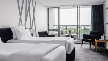 A hotel room with two beds, a balcony with a view, and a small table with chairs.
