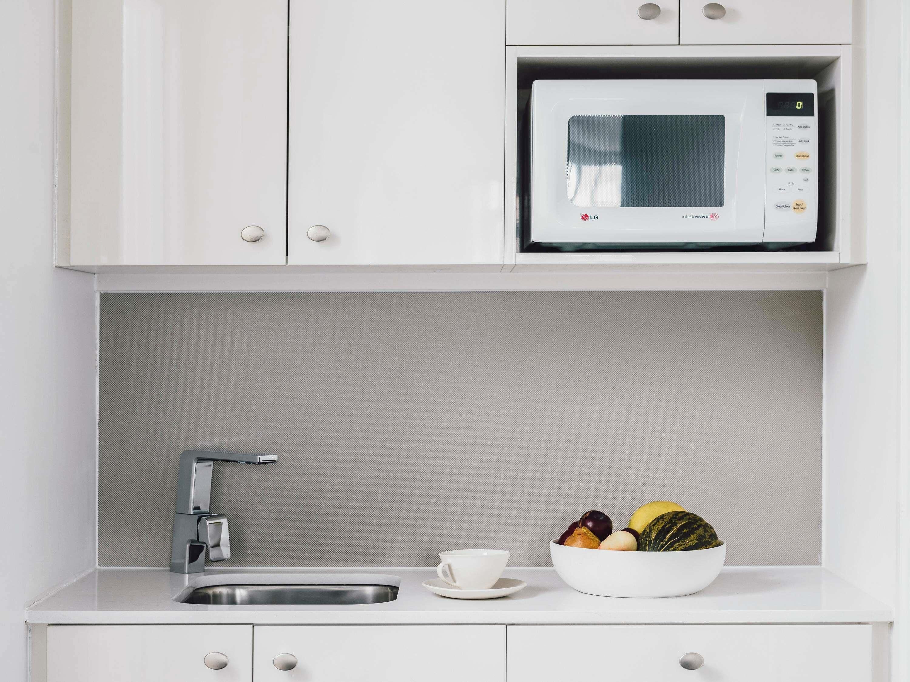 A modern kitchen with a built-in microwave, stainless steel sink, and a bowl of fruit on the counter.