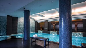 Un área de piscina interior moderna con un banco, pilares grandes y detalles decorativos en la pared.