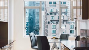 Una cocina moderna con una mesa de vidrio, dos sillas y vistas a un rascacielos a través de amplios ventanales.