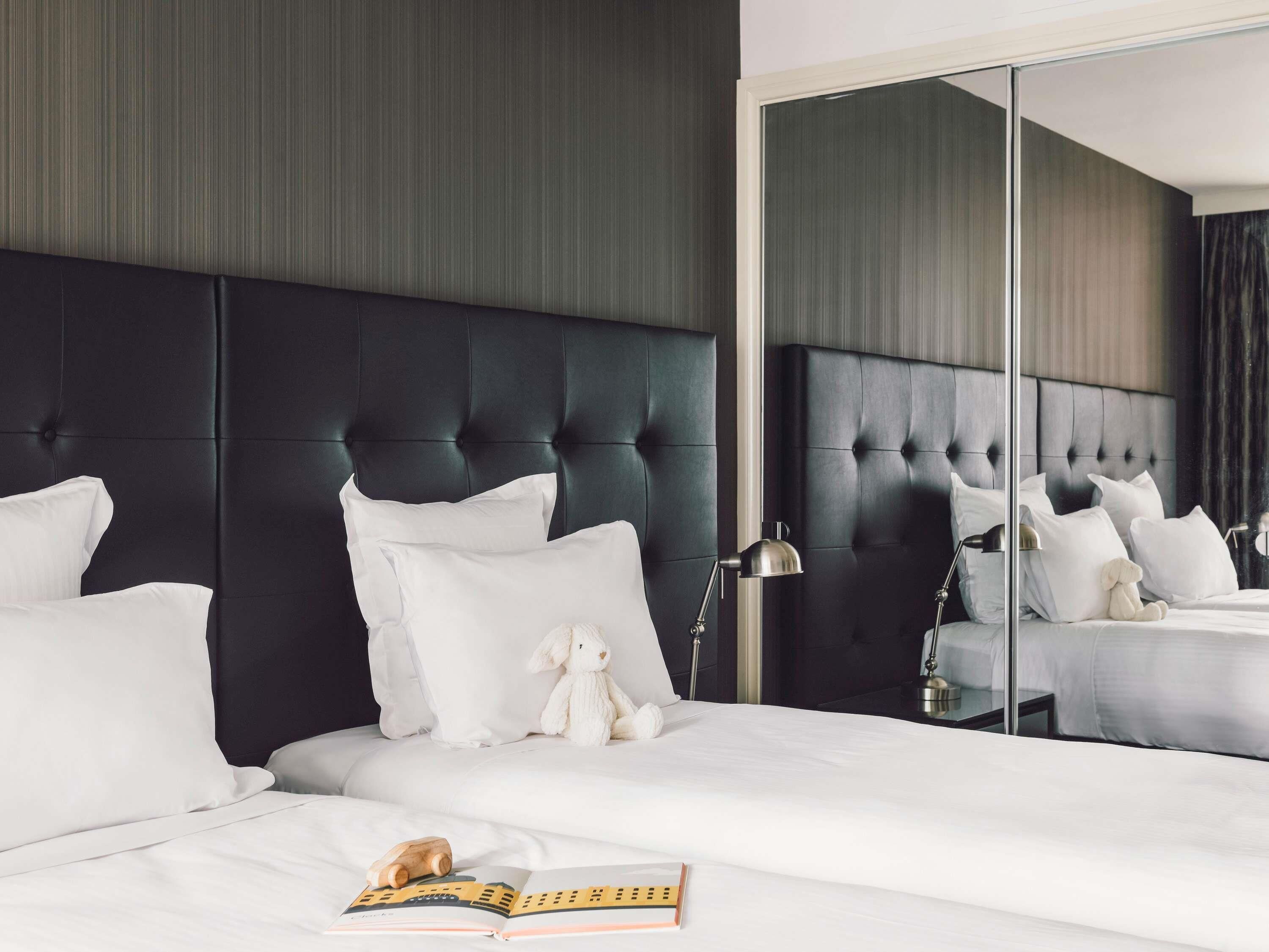 A hotel room with a large bed, a mirror, a plush toy, and a book on the bed.