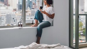 Una persona sentada junto a una ventana con vista a la ciudad, sosteniendo una taza.