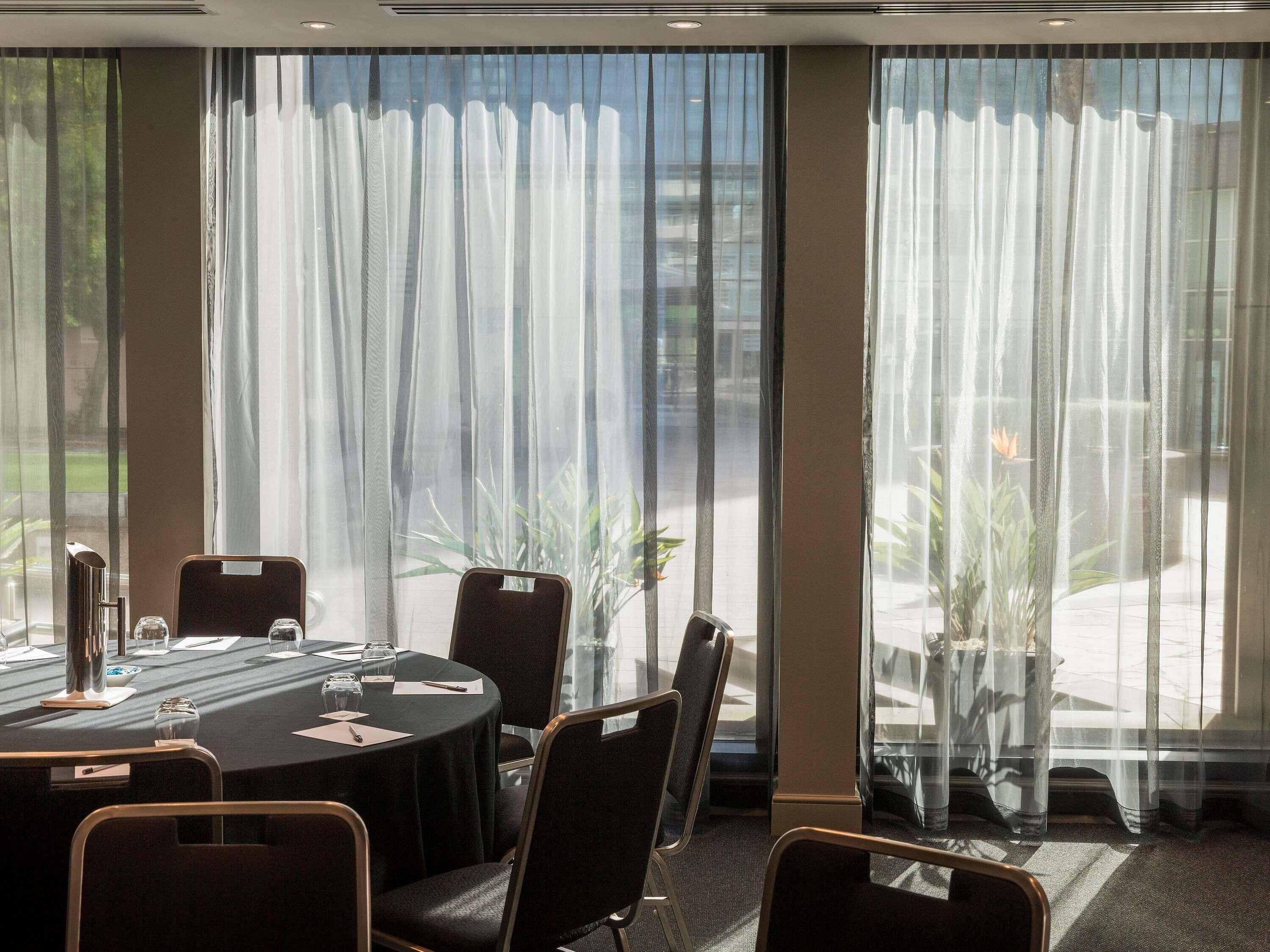 A conference room with a round table, chairs, and a large window with sheer curtains.