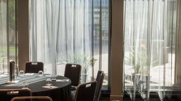 A conference room with a round table, chairs, and a large window with sheer curtains.