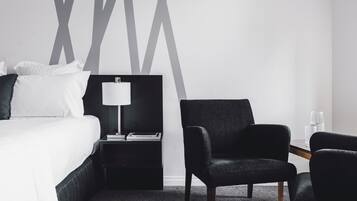 Ein Hotelzimmer mit einem Bett, einem Nachttisch mit Lampe, einem Stuhl und einem Glas Wasser auf einem Tisch.