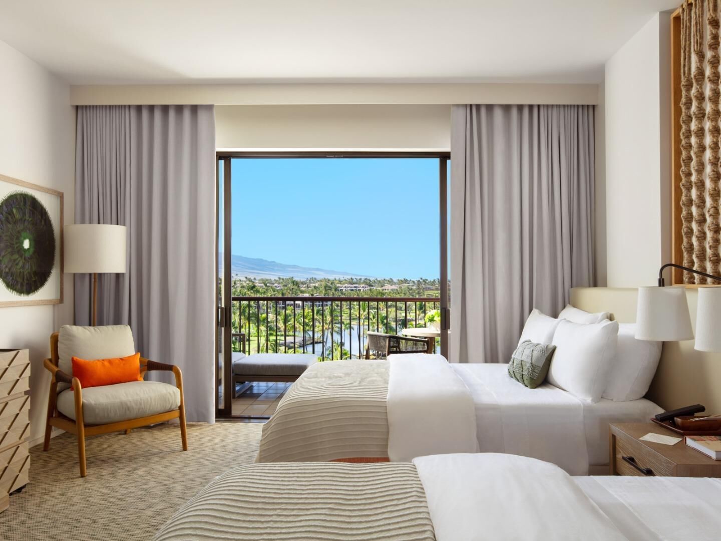 A hotel room with a bed, a chair, a desk, and a view of a pool and mountains.