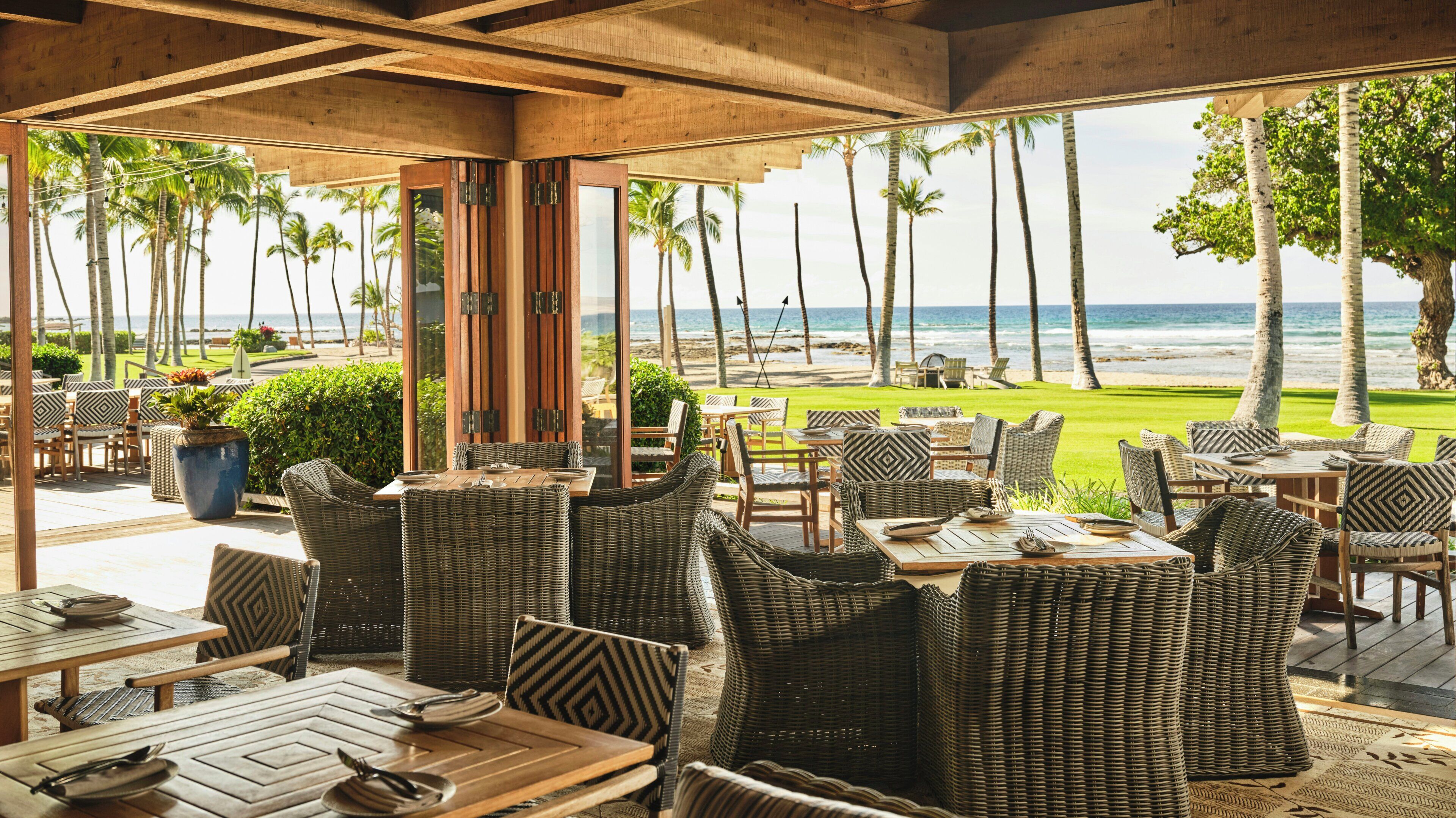 An outdoor seating area with wicker furniture, a view of the beach, and palm trees.