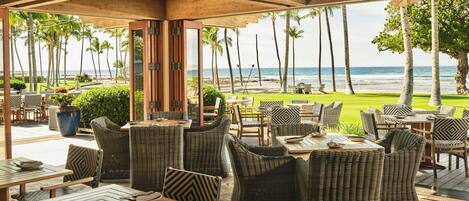 An outdoor seating area with wicker furniture, a view of the beach, and palm trees.