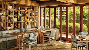 A room with a wooden ceiling, a sofa, a dining table, chairs, and shelves with various decorative items.