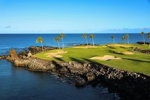 A coastal golf course with a clear view of the ocean, palm trees, and rocky terrain.